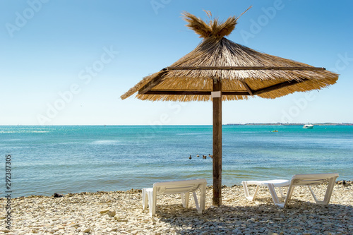 Vacation background. Two deckchairs and umbrella on a beach. Blue water of sea bay. Pebbles under your feet.