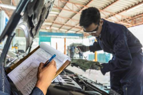 A mechanic service car in garage is check a list car and Asian man auto mechanic using a wrench to service car in garage.