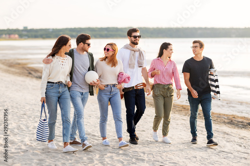 friendship, leisure and people concept - group of happy friends with ball, guitar, bag and blanket walking along beach in summer