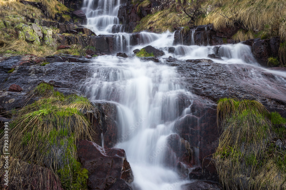 Low perspective, long exposure, close up composition of scenic Monk's jump waterfall on Old mountain, cascading down the sunlit dark red rocks Low perspective, long exposure, close up composition of scenic Monk's jump waterfall on Old mountain, cascading down the sunlit dark red rocks