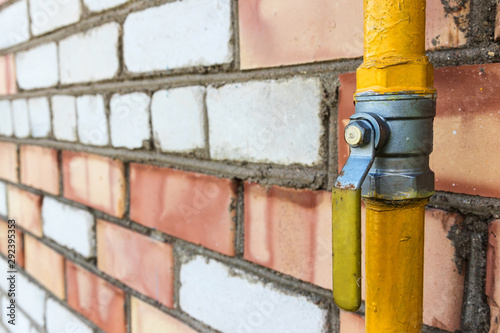 Yellow gas pipe with a crane goes along the facade of a old brick wall. House connected to gas for domestic use