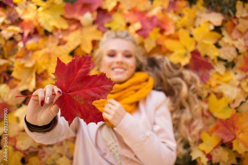 Portrait of pretty happy blonde teen girl lying on the carpet of yellow and red leaves