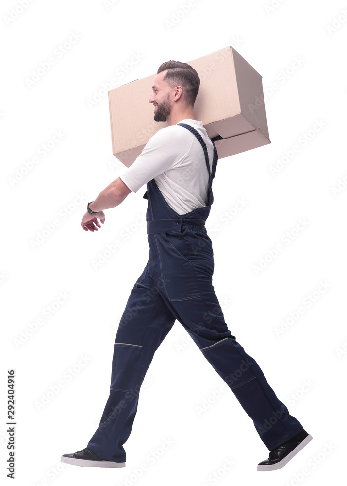side view. a man in overalls carries a large cardboard box side view. a man in overalls carries a large cardboard box