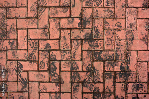 Grunge background. Many black asphalt draggled footprints on red stone block pavement/ bricks. Vertical direction of footprints