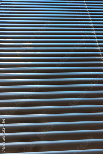 Closed aluminium roller blinds pattern and texture. Blue sky and rays of light in office window. Sunblind background.