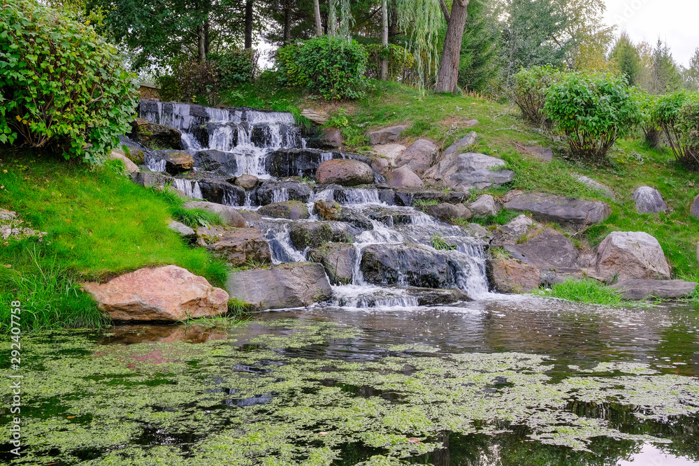 Landscape with a forest waterfall. Water runs on the rocks to the bottom forming a small pond. Landscape with a forest waterfall. Water runs on the rocks to the bottom forming a small pond.