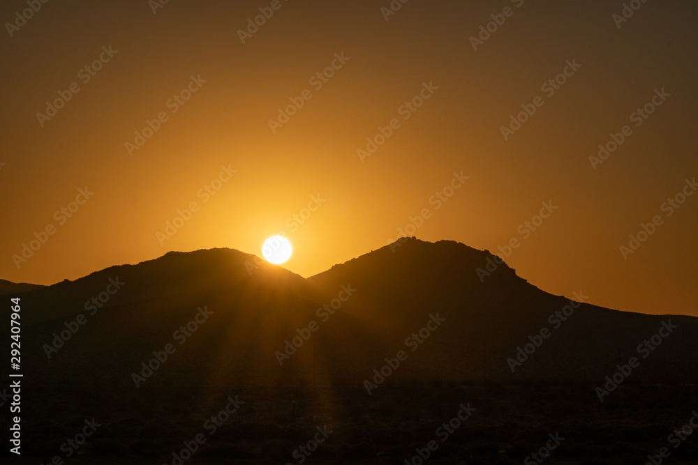 Sun peaking over mountains at sunrise in the mojave desert Sun peaking over mountains at sunrise in the mojave desert