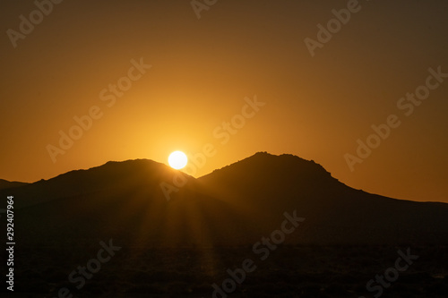 Sun peaking over mountains at sunrise in the mojave desert