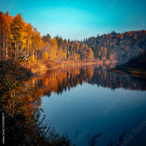 Riverside in autumn colors , Vivid morning in colorful forest with sun on trees. Scenery of nature with sunlight, autumn forest.