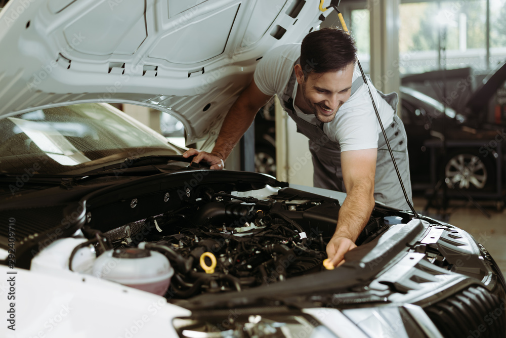 Young smiling auto mechanic examining engine in a workshop Young smiling auto mechanic examining engine in a workshop