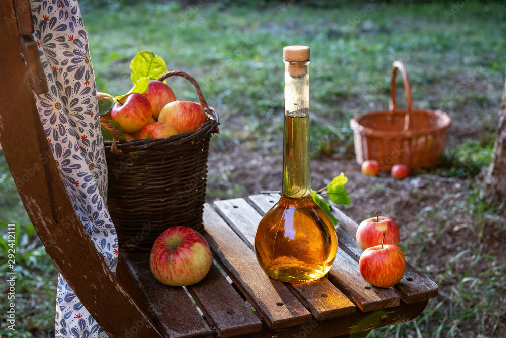 A bottle of apple cider vinegar with fresh apples, outdoors