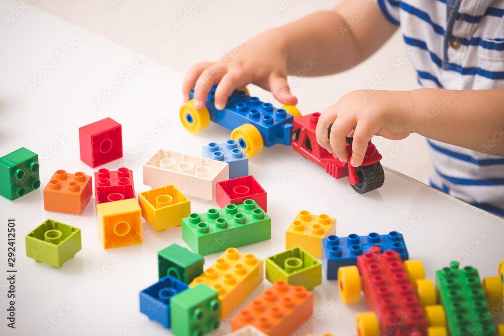 Toddler child playing multi-colored cubes on the table. Colorful plastic bricks for the early development of the child. Early learning and educational toys for a little boy - obrazy, fototapety, plakaty 