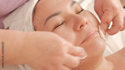 Wallpaper Mural A girl of Asian appearance on the procedure of cleansing and rejuvenating the skin in a beauty and health salon. Close-up of cosmetologist's hands wiping a female face with cotton pads. Torontodigital.ca
