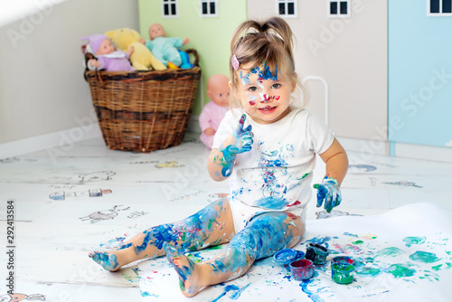 Little cute girl draws with finger paints on the floor. Early development concept