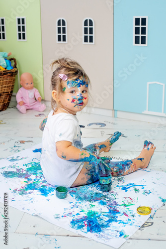 Little cute girl draws with finger paints on the floor. Early development concept