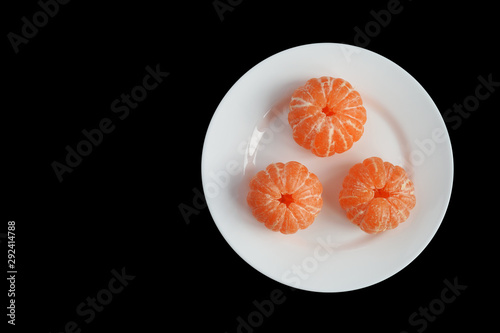 Tree different mandarins without rind on a white plate isolated on black background. Top view. Copy space