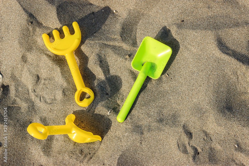 Plastic toy yellow and green shovels on beach sand in summer day. Summer vacation concept Plastic toy yellow and green shovels on beach sand in summer day. Summer vacation concept
