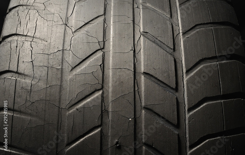 Old black tire with worn tread and cracks, worn old car tire tread, old damaged, worn black tire tread, large cracks in the car wheel, tire black color for background.