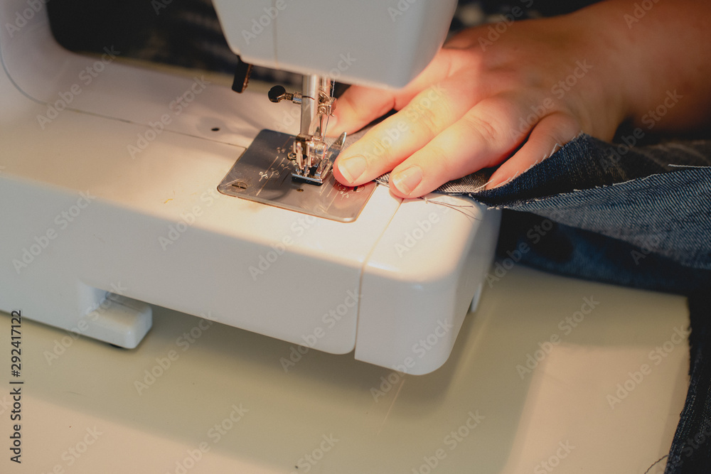 Female hands on an sewing machine sew denim. Close-up