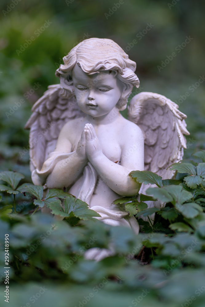 Statue of a little cherub praying as decoration on a grave Statue of a little cherub praying as decoration on a grave