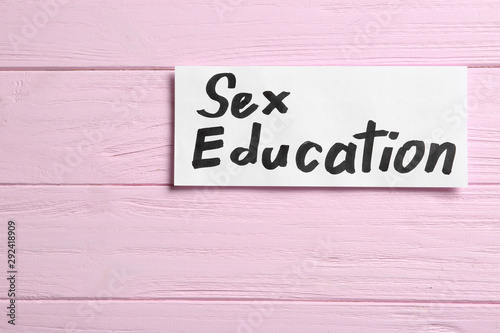 Piece of paper with phrase "SEX EDUCATION" on pink wooden background, top view