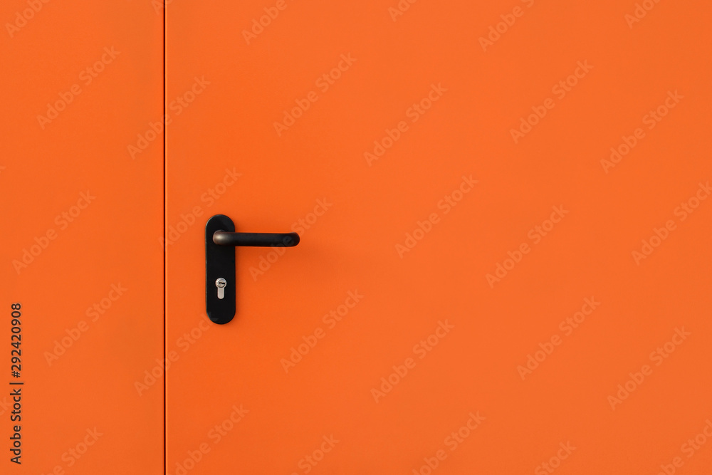 Orange modern metal door with black metal handle and turned keyhole. Copy space Orange modern metal door with black metal handle and turned keyhole. Copy space
