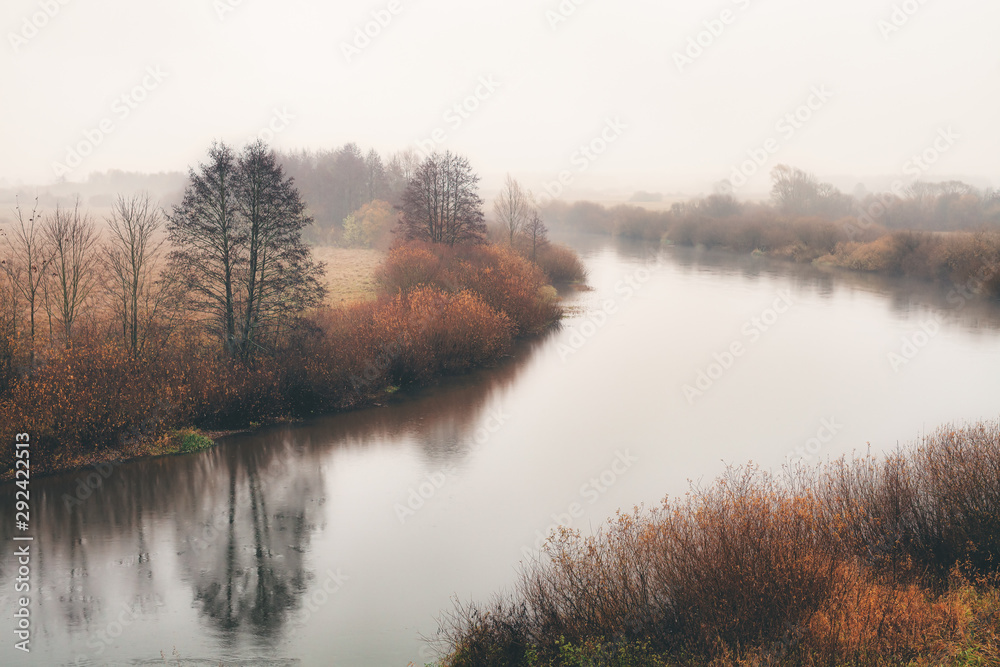Autumn landscape. A small river, fog, trees with fallen leaves.