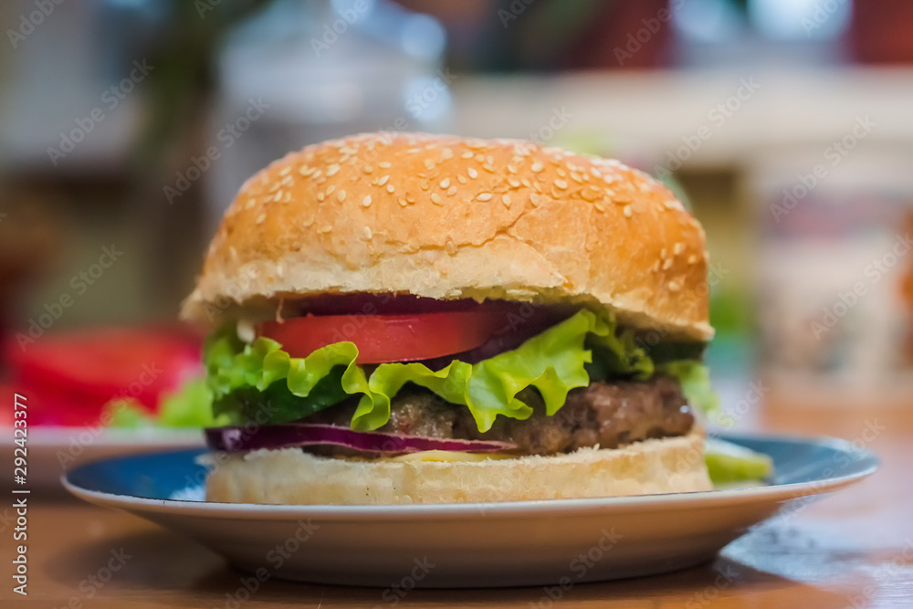 Homemade burger with tomato and beef patty, fresh toppings on whole grain artisan bun on kitchen table for dinner Homemade burger with tomato and beef patty, fresh toppings on whole grain artisan bun on kitchen table for dinner