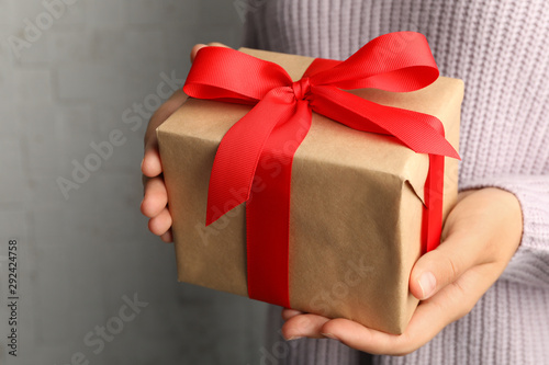 Young woman holding Christmas gift on light background, closeup