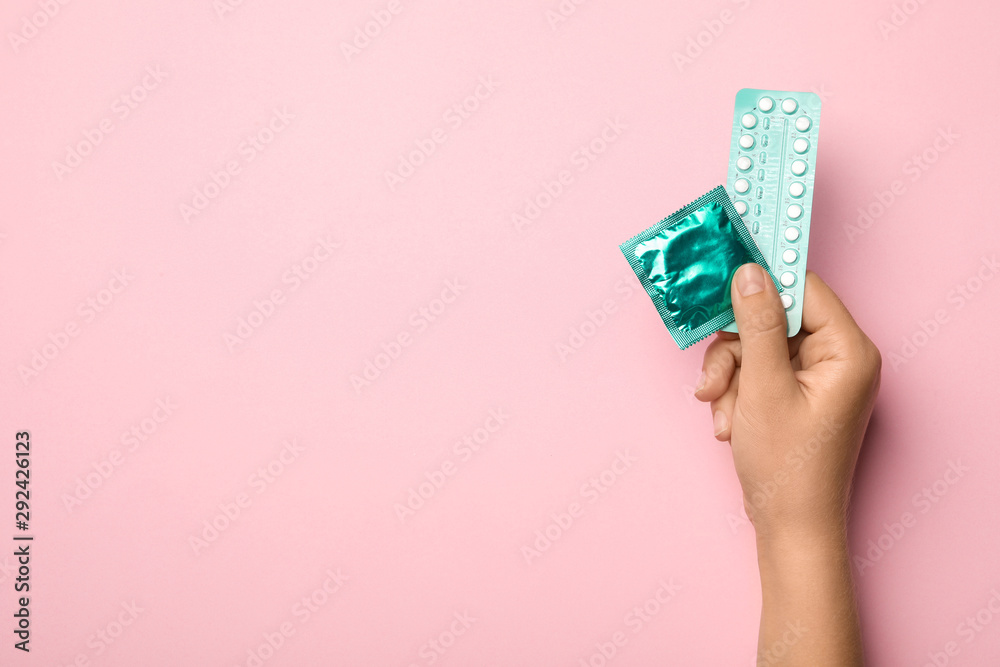 Woman Holding Condom And Birth Control Pills On Pink Background Top View With Space For Text 