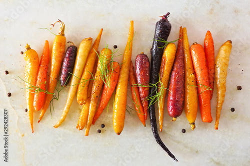 Colorful roasted rainbow carrots arranged in a row, top view over a white marble background