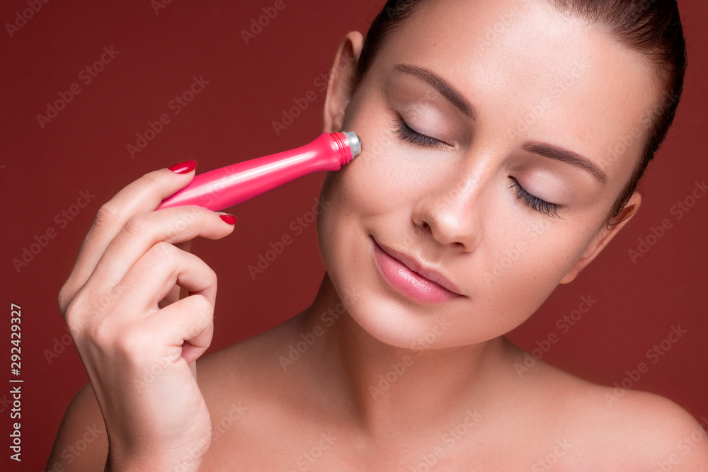 © AnnaDemy - Beautiful brunette woman massage her face with a beauty massager. Her skin fresh, clean and flawless. Spa procedure concept