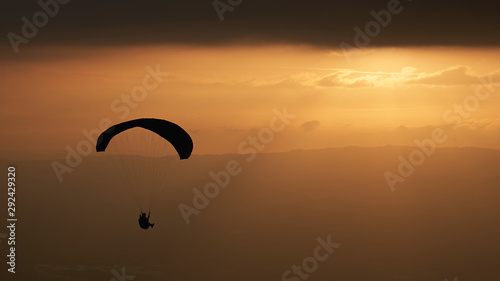One person practicing paragliding with the sunset in the background. Sun rays through the clouds. Senhora da Graça, Portugal