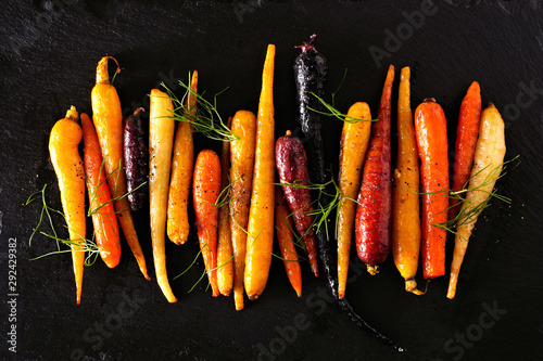 Colorful roasted rainbow carrots arranged in a row, top view over a black stone background
