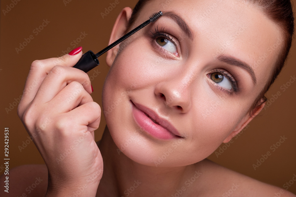 Fototapeta premium Brunette caucasian woman apply mascara with a brush. Flawless clean skin. Beauty skin care concept