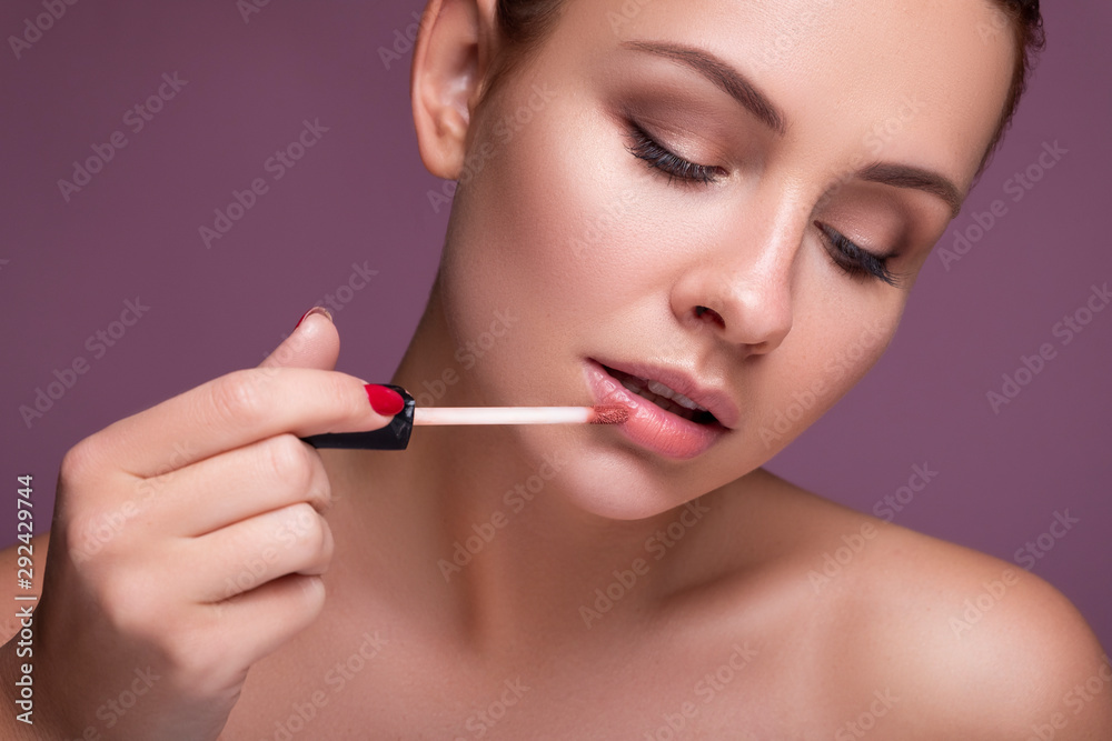 Brunette european woman apply lipstick on her lips on pink neutral background. Flawless clean fresh skin. Beauty process concept Brunette european woman apply lipstick on her lips on pink neutral background. Flawless clean fresh skin. Beauty process concept