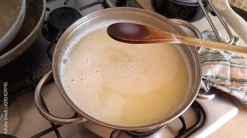 Preparing home made laundry detergent with grated Marseiile hard soap boiling it in water in a pot in the kitchen. Stirring and showing on the spoon its consistency