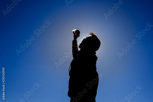 Backlit sportsman drinking water after exercising. Blue sky background.