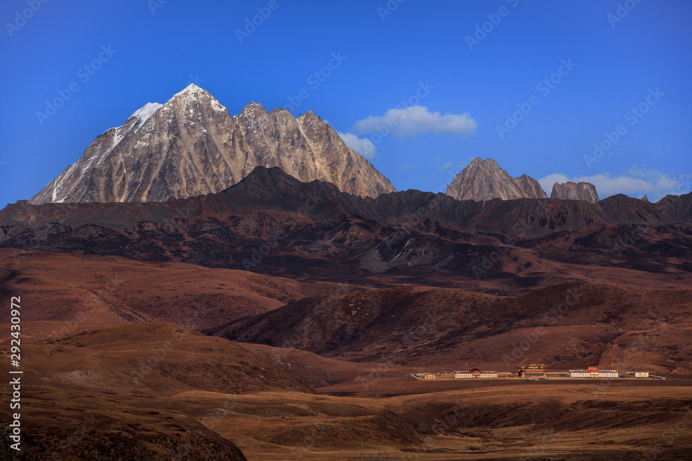 Fototapeta premium Tagong Prairie Grassland, Lhagang Grassland, Tibetan area of Sichuan Province China. Buddhist Monastery in foreground, Yala Snow Mountain towering in the distance. Strange Martian Landscape