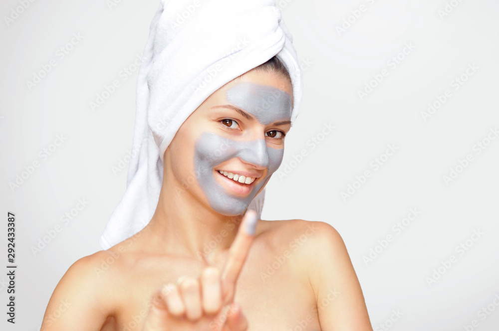 Beautiful young woman with a gray cosmetic mask on her face and a white towel on her head with bare shoulders. Beautiful young woman with a gray cosmetic mask on her face and a white towel on her head with bare shoulders.
