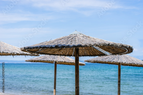 Parasol sunshade umbrella at the beach from natural materials of wood and reed cane bulrush against a sea in a sunny day at tourist destination in greece