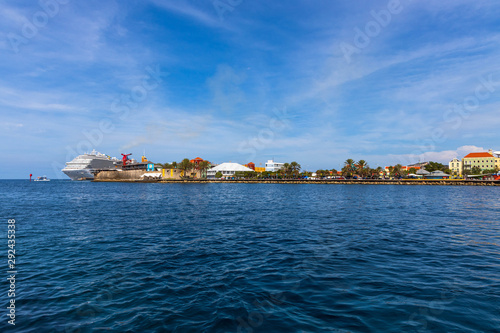 Beautiful view of coast line of Willemstad. Dark blue water surface of Atlantic ocean. Coast line with buildings and big cruise boat merging with blue sky and white clouds. Willemstad. Curasao