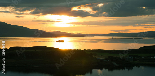 Sunset over sea from Pulpit Hill, Oban. West coast of Scotland. Isle of Kerrera in foreground and ferry sailing from Isle of Mull backlit in background. Argyll and Bute. UK. Landscape. Seascape