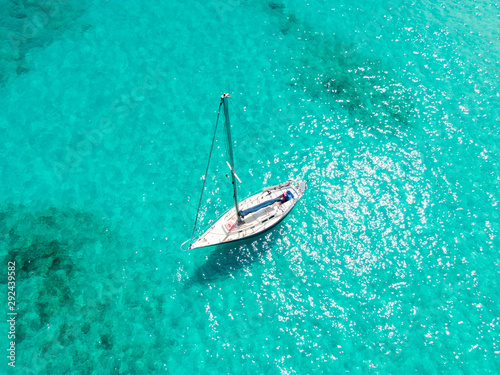 High angle aerial drone bird's eye view of a sailing yacht with sails lowered anchored in shallow, turquoise water in the Atlantic Ocean near the coast of Fuerteventura, Canary Islands, Spain, Europe. © Juergen Wallstabe