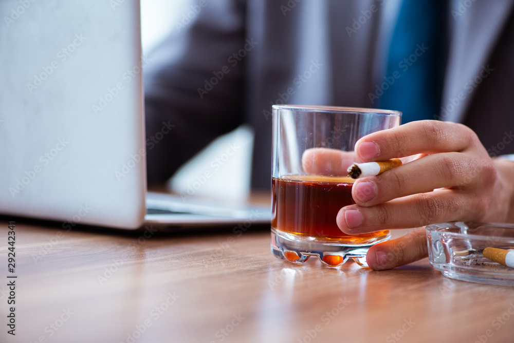 Male employee drinking alcohol and smoking cigarettes at workpla Male employee drinking alcohol and smoking cigarettes at workpla