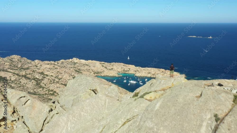 View from above, stunning aerial view of a person on the top of a granite mountain. Cala Coticcio also known as Tahiti in the background. La Maddalena Archipelago, Sardinia, Italy. View from above, stunning aerial view of a person on the top of a granite mountain. Cala Coticcio also known as Tahiti in the background. La Maddalena Archipelago, Sardinia, Italy.