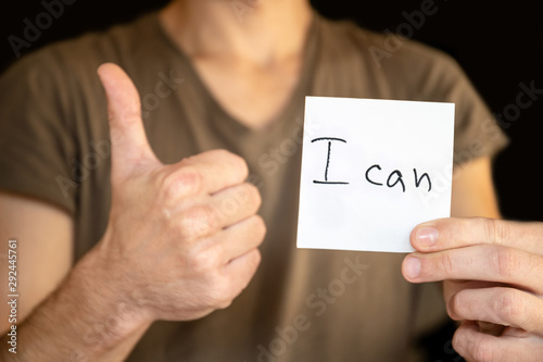 A man holds in his outstretched hand a sheet with the inscription "I can" and shows the sign of like
