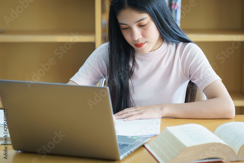 Young Asian woman student study and take notes with book in library. © EduLife Photos