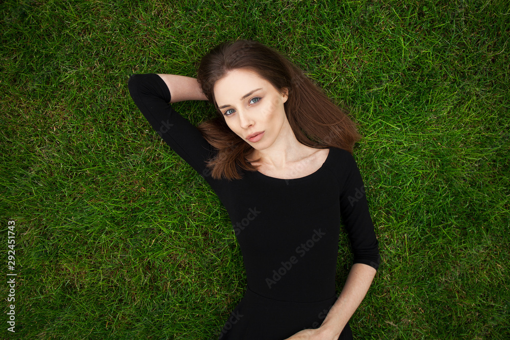 Top view portrait of a young beautiful woman in black dress lies on green lawn in a park Top view portrait of a young beautiful woman in black dress lies on green lawn in a park