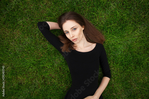 Top view portrait of a young beautiful woman in black dress lies on green lawn in a park